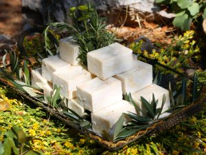 A pyramid of square, handmade soap bars displayed on a decorative tray with olive branches and yellow wildflowers.