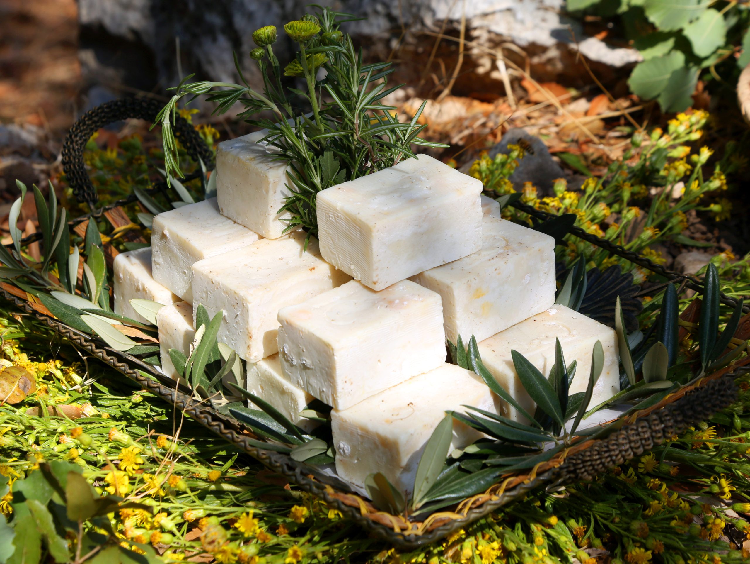 A pyramid of square, handmade soap bars displayed on a decorative tray with olive branches and yellow wildflowers.